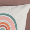 Kussen met kleurrijke regenboogprint tegen bruine muur.